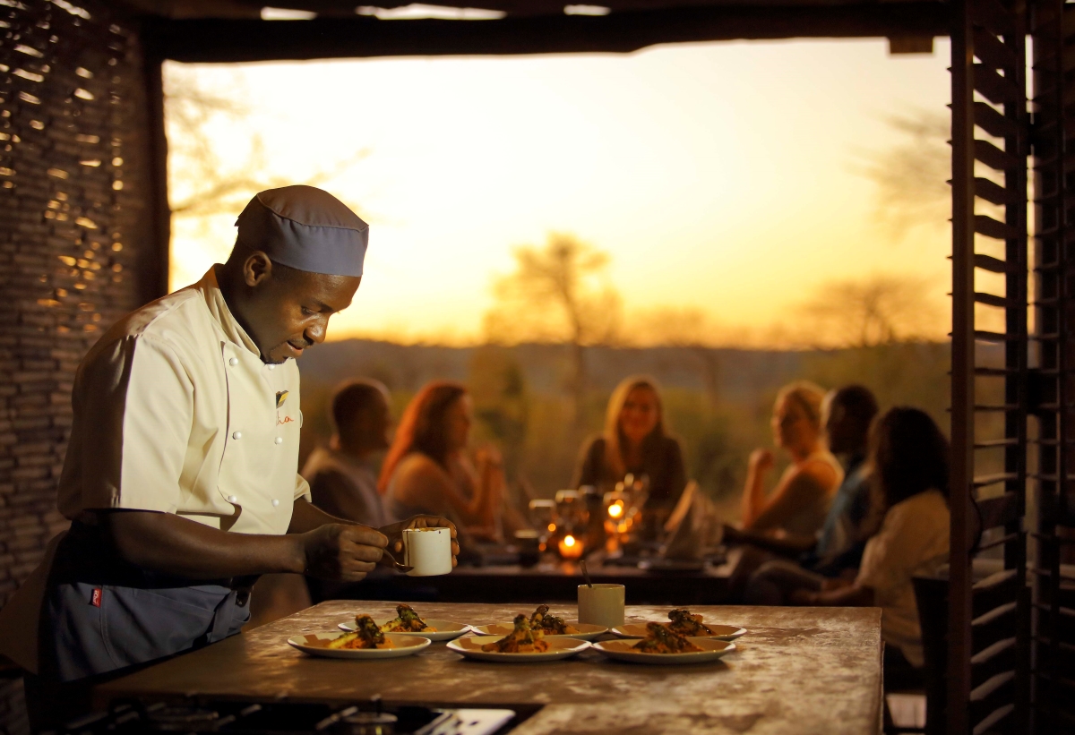 Chef preparing a late lunch while a family enjoys drinks and catching up around an outdoor dining table