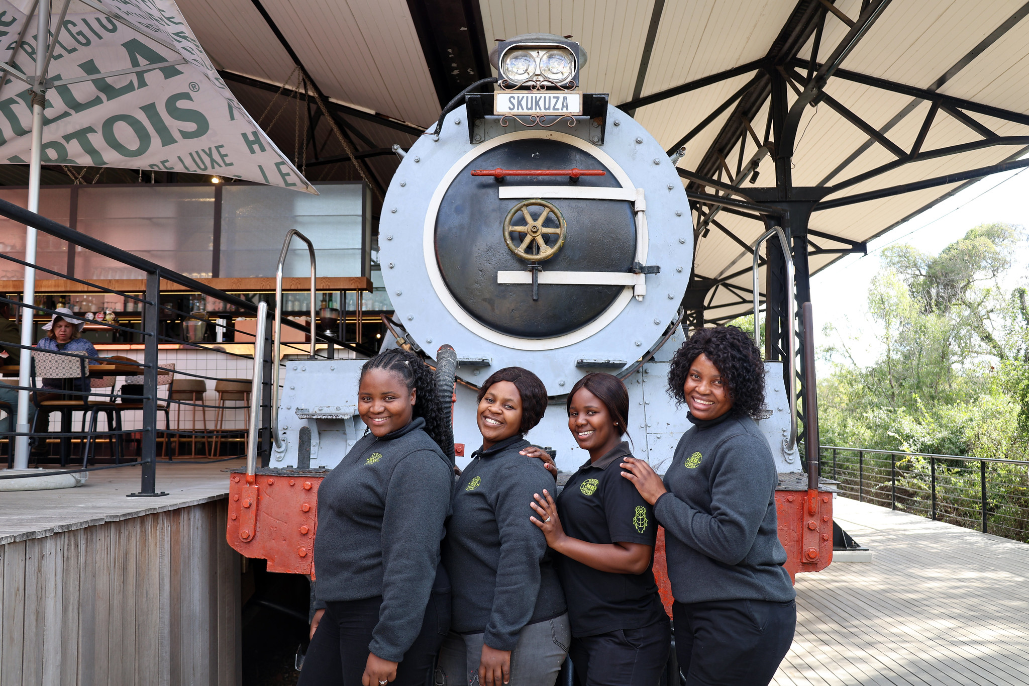 Image of Lwazi Thobela, Noxolo Mathebula, Vutivi Mthimkhulu and Mampho Makofane posing in front of a stationary train at the Kruger Station restaurant 